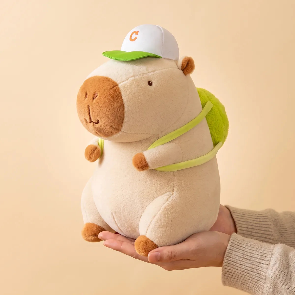 Hand holding the white tennis backpack capybara plush to show its real size