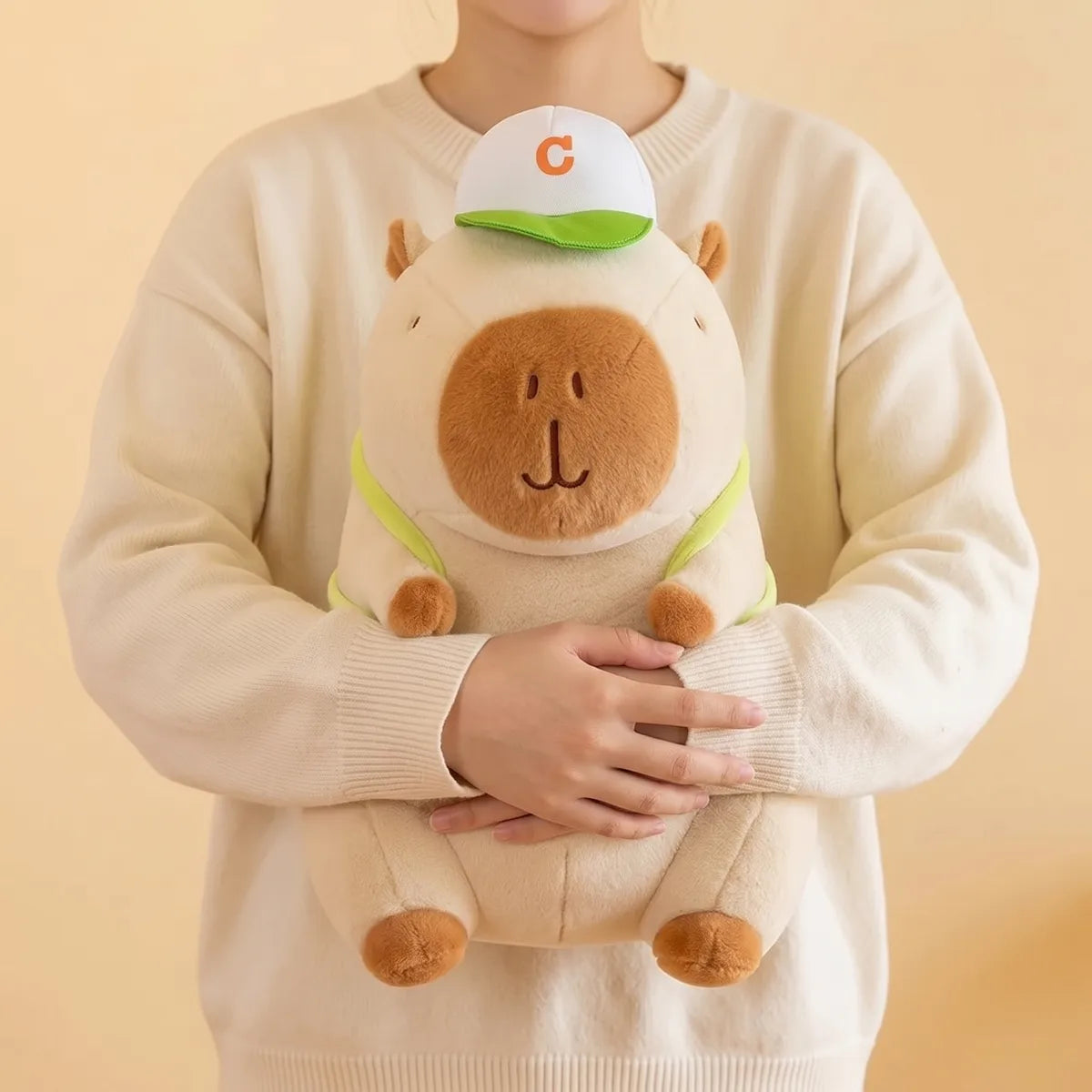 Person hugging the white tennis backpack capybara plush against a cream knit sweater
